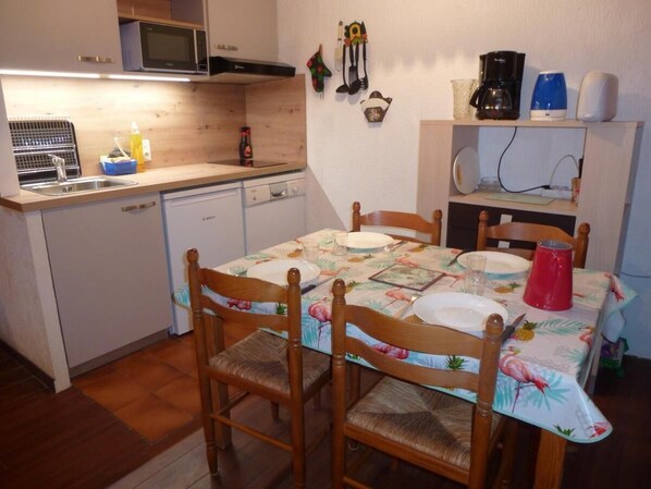 Une cuisine compacte avec des meubles en bois, un four à micro-ondes et une table à manger pour quatre personnes, agrémentée de nappes à motifs floraux.