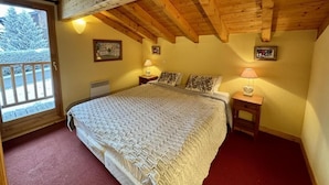 Ein Schlafzimmer mit einem großen Bett, Holzbalkendecke, einem Fenster mit Blick auf Bäume und zwei Nachttischen mit Lampen.