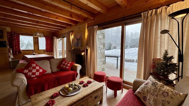 Ein gemütliches Cabin-Interieur mit Holzbalkendecke, einer Sofagarnitur, einem Esstisch und Blick auf eine verschneite Landschaft durch große Fenster.