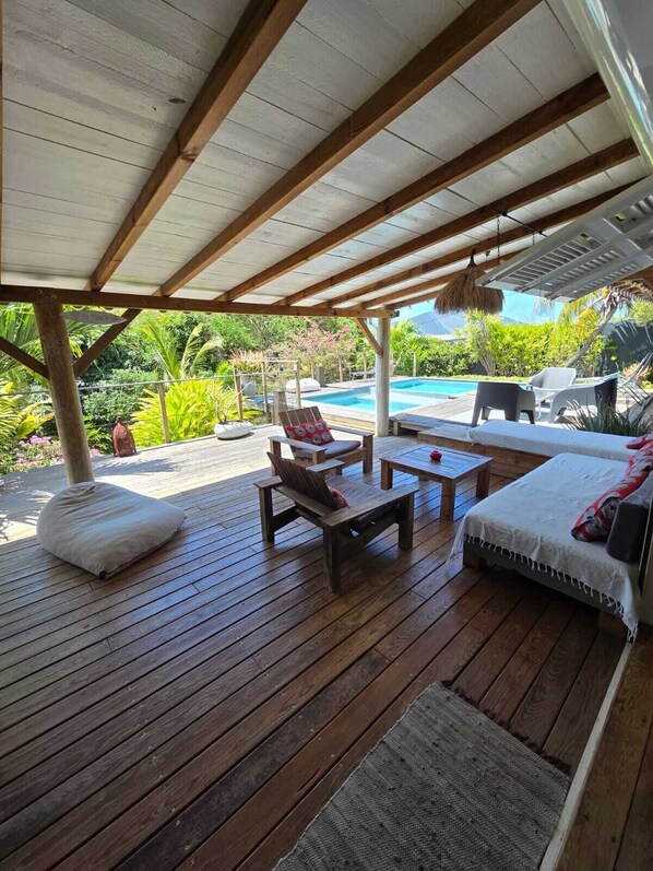 Una terraza exterior con piso de madera, piscina y zona de estar con sofá y sillones.
