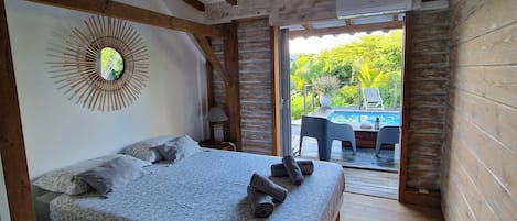 A bedroom with a wooden ceiling, a bed with a floral bedspread, and a view of an outdoor area with a table and chairs.