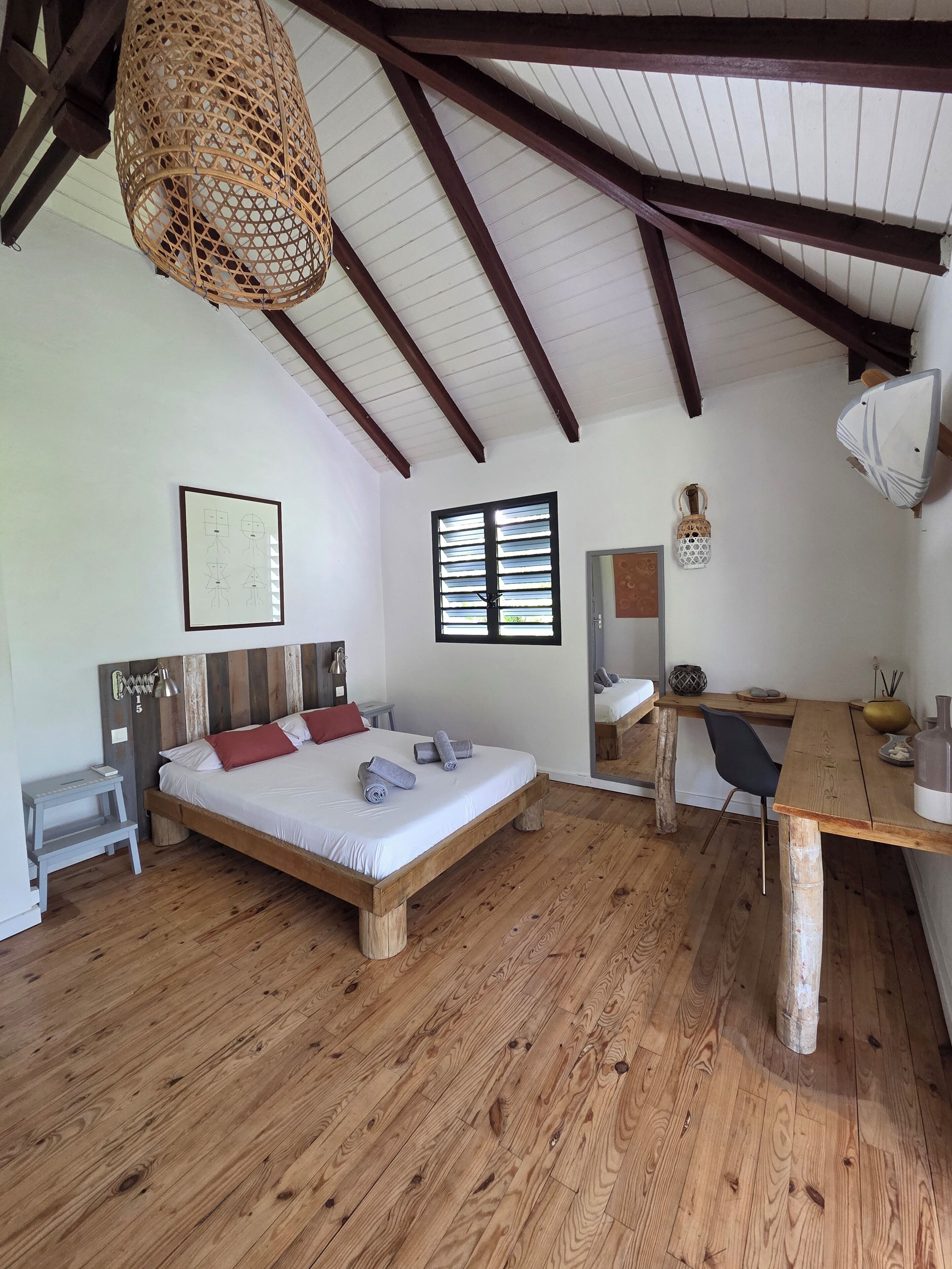 A room with a wooden bed, a desk, a chair, a hanging light fixture, and a window with blinds.