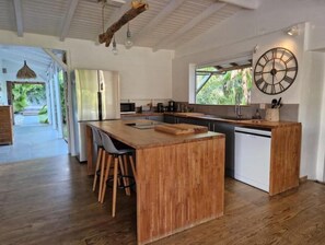 A modern kitchen with a central island, wooden stools, and a large wall clock. - Sublime Villa Makiesé Dans son Jardin Tropical (Saint-François)