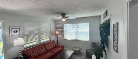A living room with a red leather sofa, a coffee table, a floor lamp, and a ceiling fan.