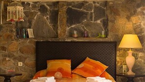 A bed with an orange bedspread, a stone wall, a hanging light fixture, and a nightstand with a lamp. - Seaview villa w/private pool near Elafonissi beach (Chania)