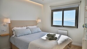 Een slaapkamer met een bed, twee bedlampen, een raam met uitzicht op zee en een plafondventilator.
