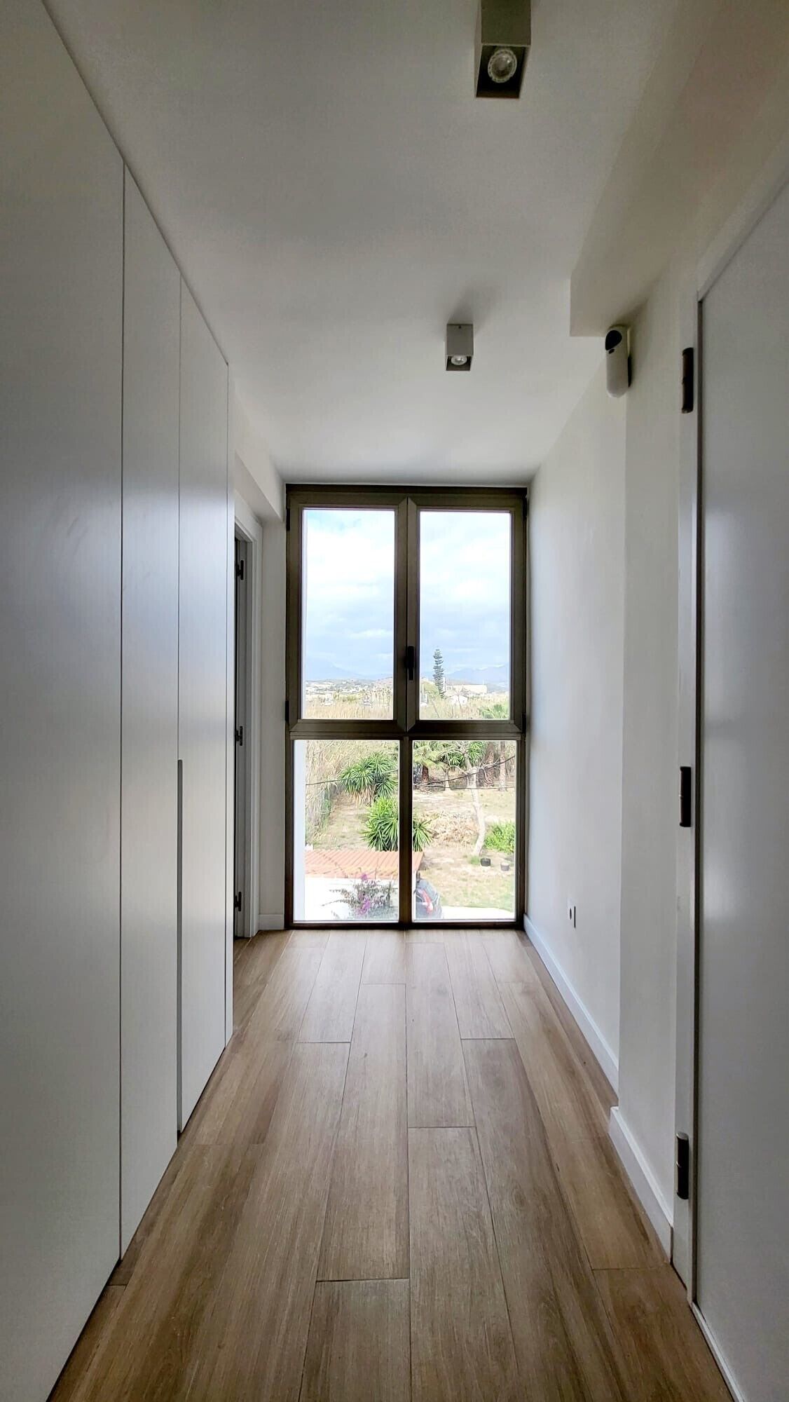 Un couloir avec une grande porte-fenêtre coulissante donnant sur un balcon qui offre une vue sur un quartier résidentiel.