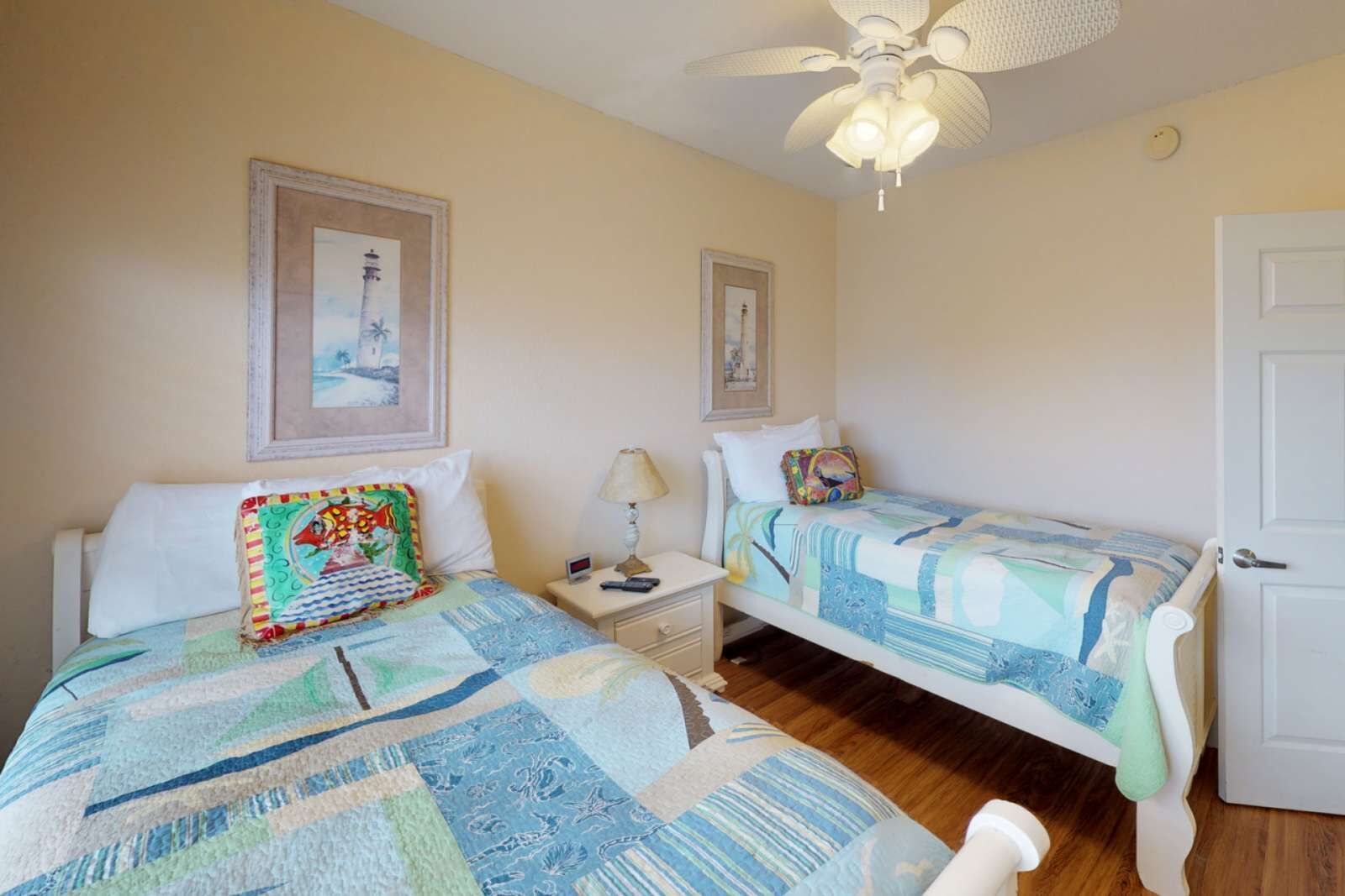 A bedroom with two beds, a ceiling fan, and framed pictures on the walls.