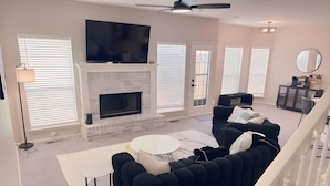 A modern living room with a fireplace, black sofas, a flat-screen TV, and a staircase. - 4 bedrooms+Outdoor gazebo+Garage+office (Tulsa)