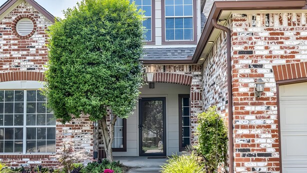 A two-story house with a brick facade, a front porch, and a well-maintained garden with various plants and flowers. - 4 bedrooms+Outdoor gazebo+Garage+office (Tulsa)