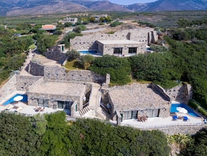 A stone villa with multiple swimming pools, surrounded by lush greenery and mountains.