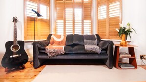 Ein Wohnzimmer mit einer schwarzen Couch, einer Gitarre, einer Lampe und einem Bücherregal.