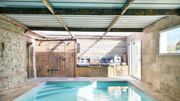 A swimming pool with a brick wall and wooden door, a covered patio area with cushions, and a view of the outside. - Inédit! Spa, Piscine, Salle de Jeux (La Poterie-Cap-d'Antifer)