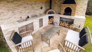 An outdoor kitchen with a stone wall, a brick oven, and a grill. - Inédit! Spa, Piscine, Salle de Jeux (La Poterie-Cap-d'Antifer)