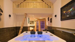 A hot tub in a room with a wooden staircase, a painting on the wall, and a view into another room. - Inédit! Spa, Piscine, Salle de Jeux (La Poterie-Cap-d'Antifer)