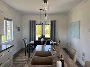 A modern kitchen with a double sink, dining area with a table and chairs, and a view of greenery outside. - Stunning Ocean View Home (Summerford)