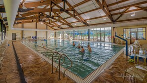 An indoor swimming pool with a high ceiling and wooden beams, surrounded by lounge chairs and a view of the outdoors. - House 3bd-3bth-fire pit-screen porch-outdoor pool - close to everything (Galena)