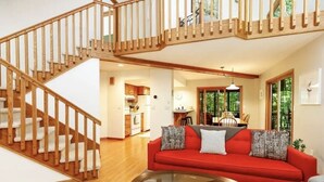 A spacious living area with a wooden staircase, a red sofa, and a glass coffee table. - House 3bd-3bth-fire pit-screen porch-outdoor pool - close to everything (Galena)