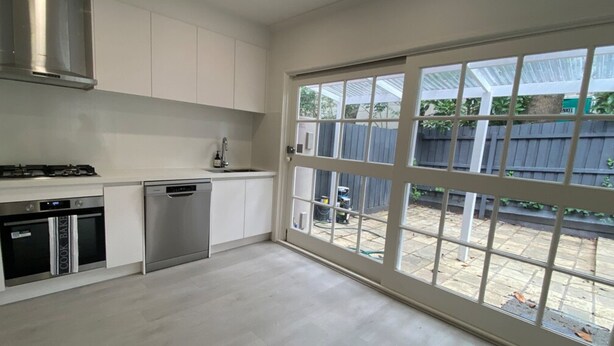 Una cocina moderna con armarios blancos, electrodomésticos de acero inoxidable y un amplio ventanal corredera que da a un jardín trasero.