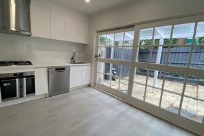 Una cocina moderna con armarios blancos, electrodomésticos de acero inoxidable y un amplio ventanal corredera que da a un jardín trasero.