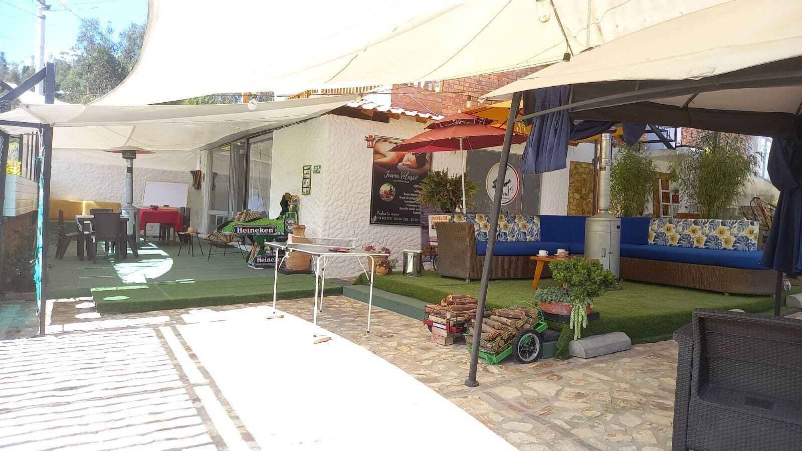 Ein Außenbereich mit Terrassengarten, einem überdachten Sitzbereich, einem Tisch und einem kleinen Wagen mit Brennholz.