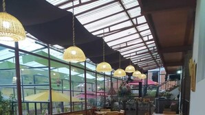 Un'ampia sala da pranzo con tavoli e sedie in legno, ampie finestre che offrono vista sul paesaggio circostante e lampade a sospensione in vimini.
