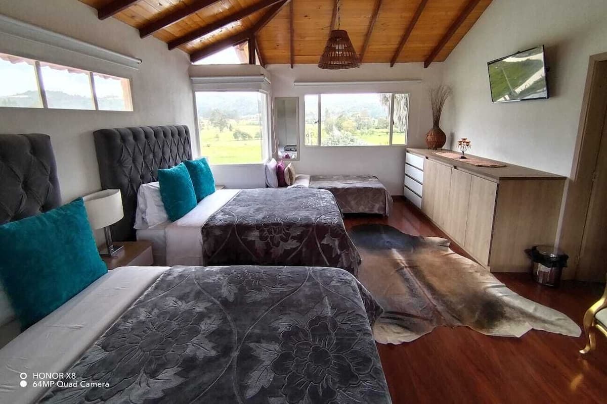 A bedroom with two beds, a wooden ceiling, a large window, and a view of the outdoors.