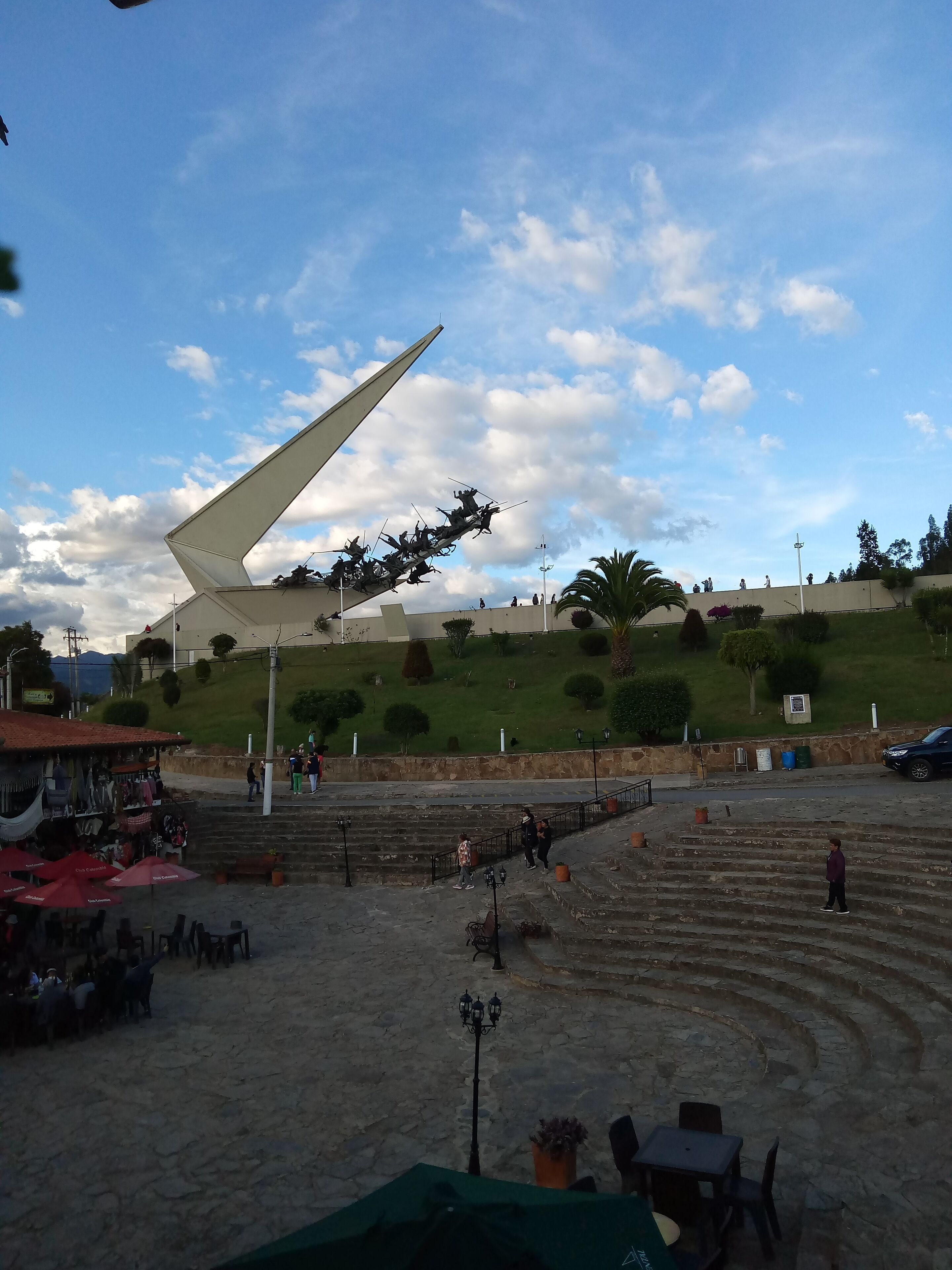 Una plaza pública con una gran escultura, escalones y una zona de café.