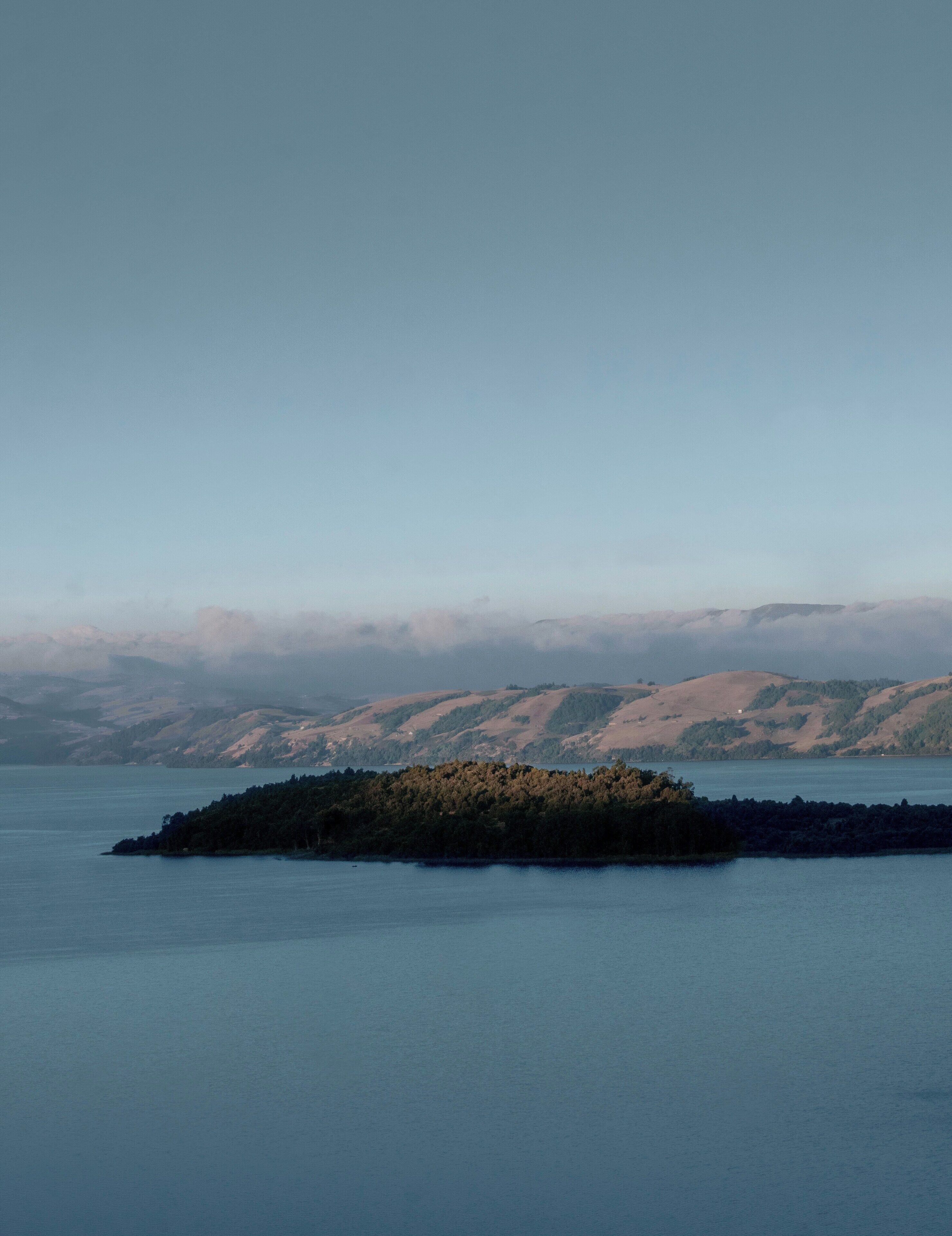 Un lago tranquilo con una pequeña isla al frente y un paisaje montañoso en el fondo.