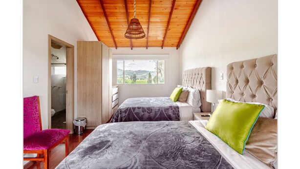 Una camera da letto con due letti, un soffitto in legno, una finestra vista e una sedia.