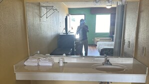 A bathroom with a large mirror, a sink, and a towel rack. - American Inn (Sumter)