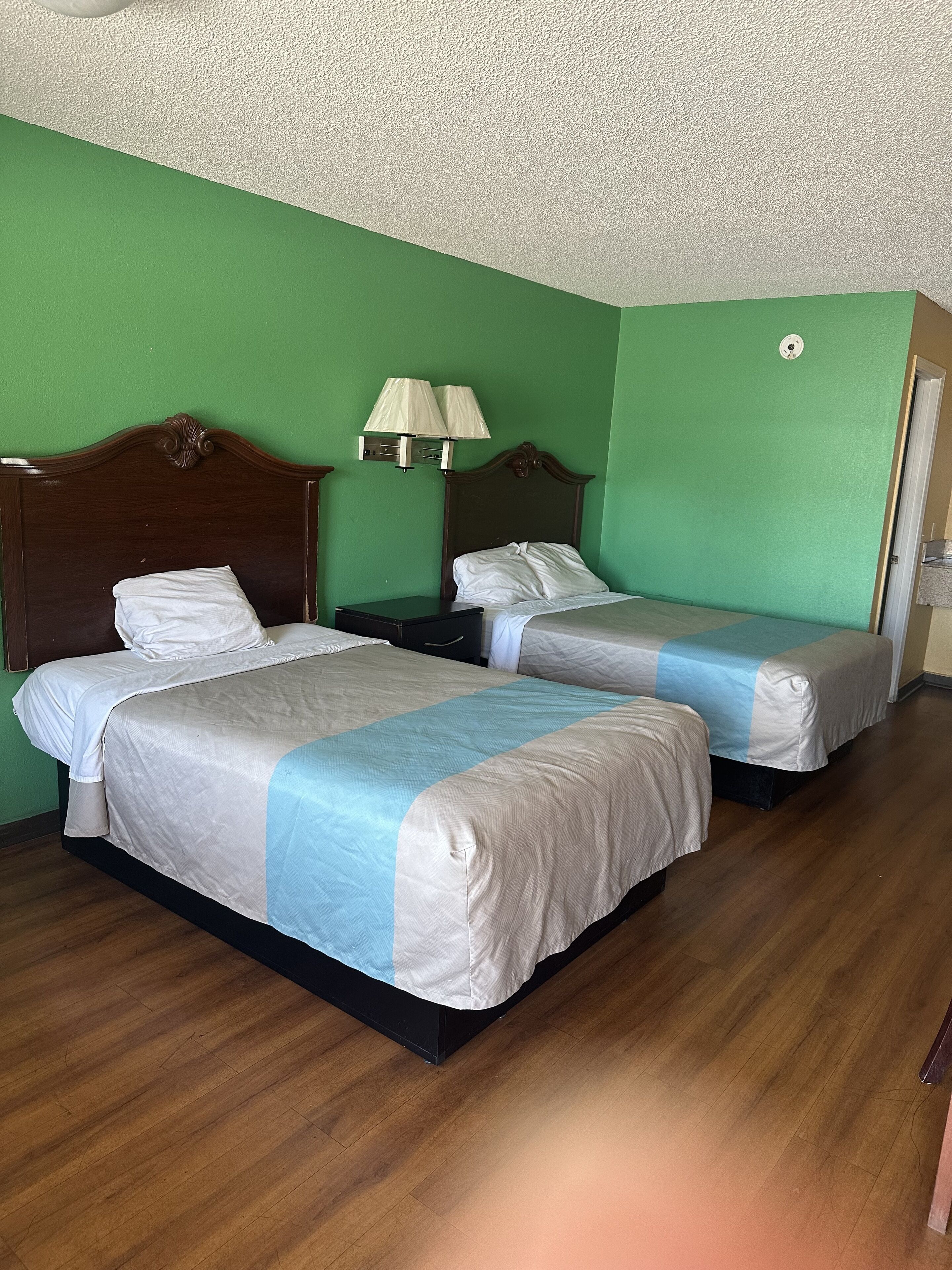 A room with two beds, green walls, wooden flooring, and a ceiling with a textured finish.