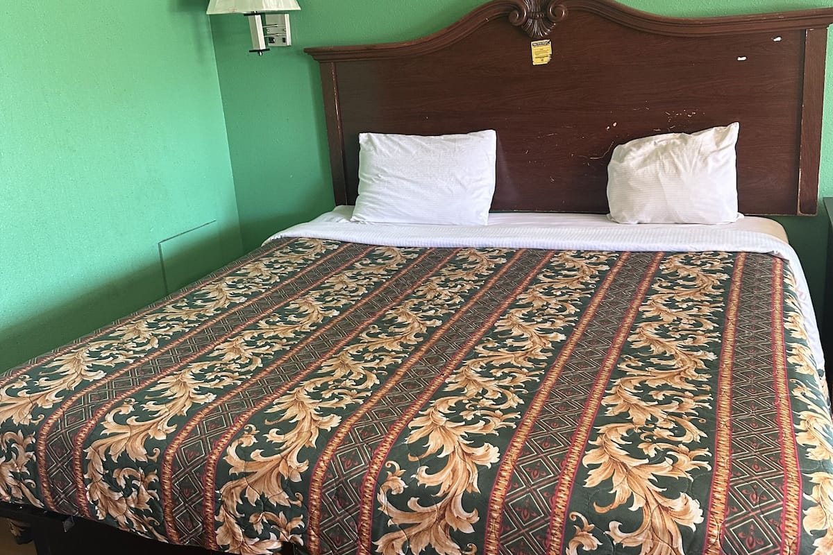 Uma cama com colcha estampada, cabeceira de madeira e luminária na parede.