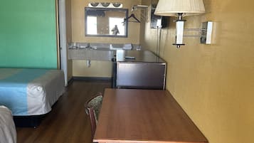 A compact hotel room with a single bed, a small kitchenette, a dining table, and a mirror.