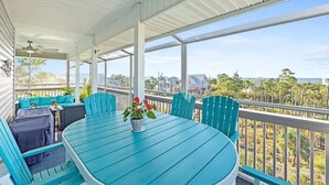 Un espace extérieur aménagé, abrité, avec une table et des chaises, un pot de fleurs et une vue sur l’océan et les bâtiments.