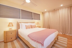 A neatly arranged bedroom with a bed, two bedside tables with lamps, a window with blinds, and a curtain.