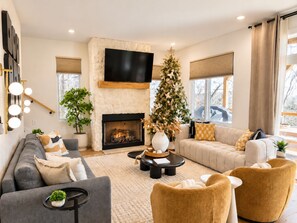 A modern living room with a fireplace, a large flat-screen TV, a Christmas tree, and comfortable seating.
