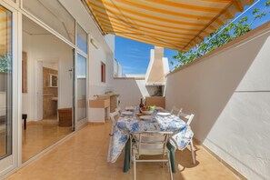 Enjoy al fresco dining under a shaded patio with a dining table for two, a bowl of fresh fruits, and a bottle.