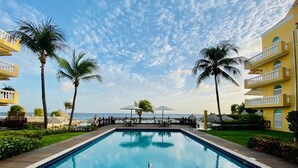 Zona de piscina con vistas despejadas al océano, rodeada de palmeras y una terraza de madera.