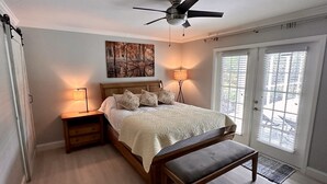 A bedroom with a bed, bedside lamps, a ceiling fan, a bench, and a view through a door. - Private house with heated pool in the custom tropical garden.
 (Naples)