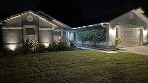 A residential house with a well-lit front yard, a landscaped garden, and a garage. - Private house with heated pool in the custom tropical garden.
 (Naples)
