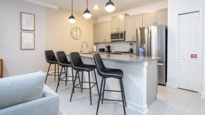 A modern kitchen with a central island, stainless steel appliances, and black bar stools. - Beautiful & Cozy Home at Storey Lake Resort (Kissimmee)