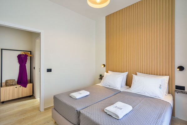 Habitación de hotel con dos camas, cabecero de madera, armario y perchero.