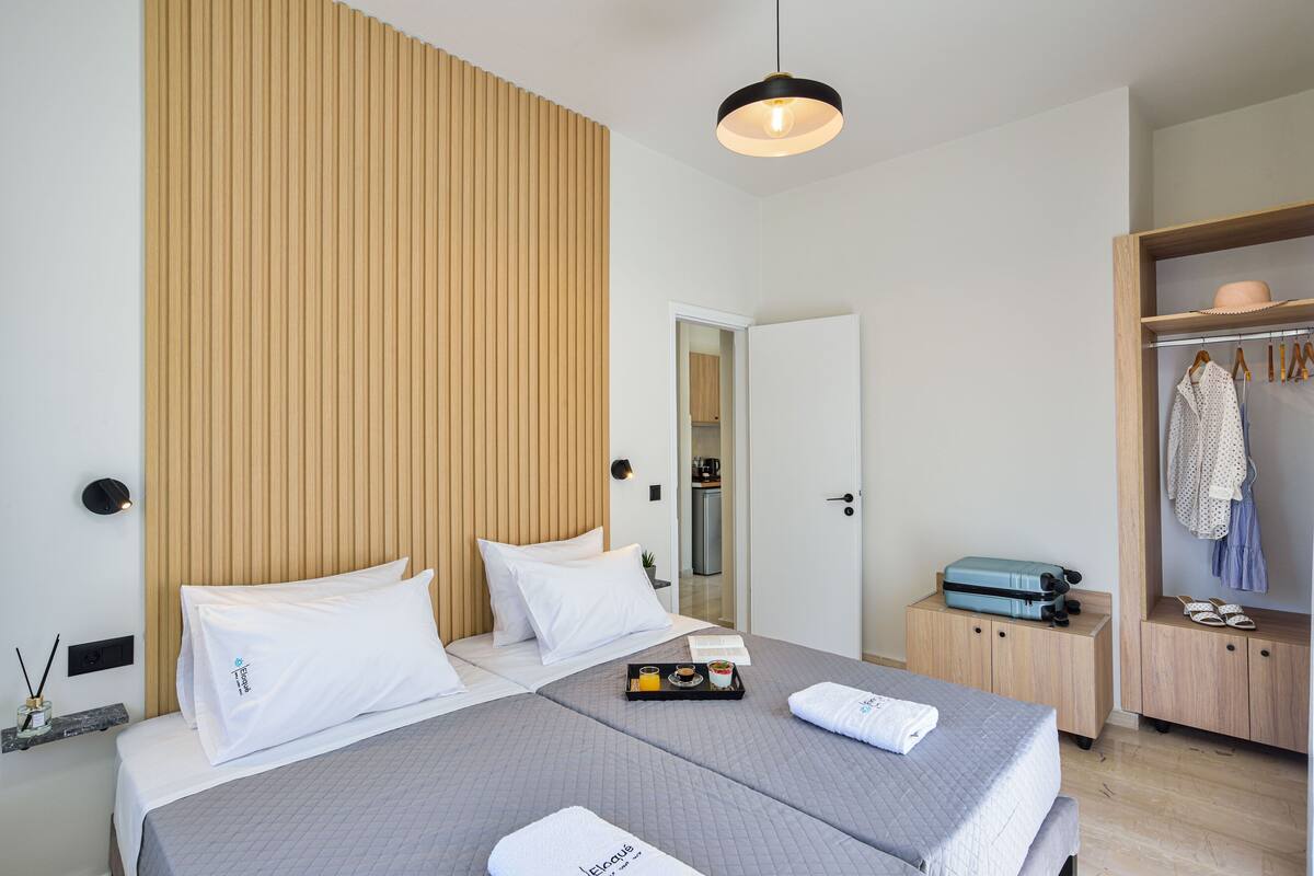 A hotel room with two beds, a wooden headboard, a bedside table with a tray of breakfast, and a wardrobe with hanging clothes.