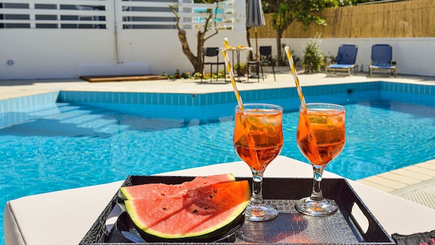 Escena a la piscina amb una taula que té dues begudes i una làmina de meló.