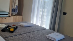 Habitació d'hotel amb un llit, un armari, una taula petita amb un plat de desig i una finestra amb cortines.