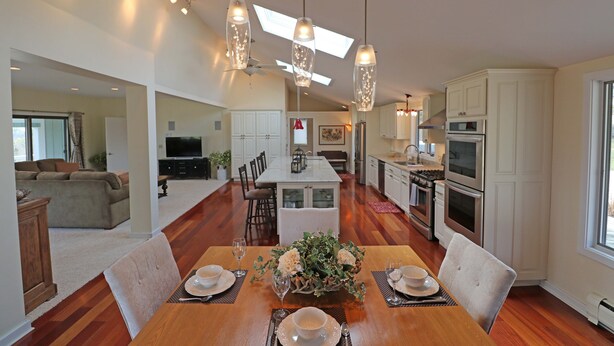 A spacious kitchen with modern appliances, a dining area with a wooden table set for four, and a living area with a sofa and television.