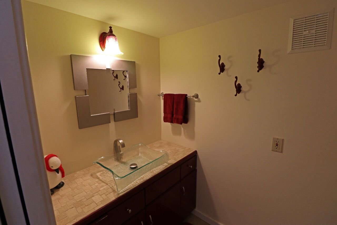 A bathroom with a glass sink, a mirror, a red towel, and wall-mounted hooks.