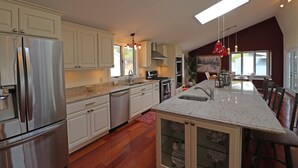 A modern kitchen with white cabinets, stainless steel appliances, a large island with a sink, and a red pendant light.