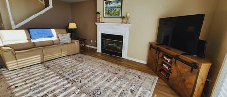 A living room with a sofa, a fireplace, a television, and a patterned rug.